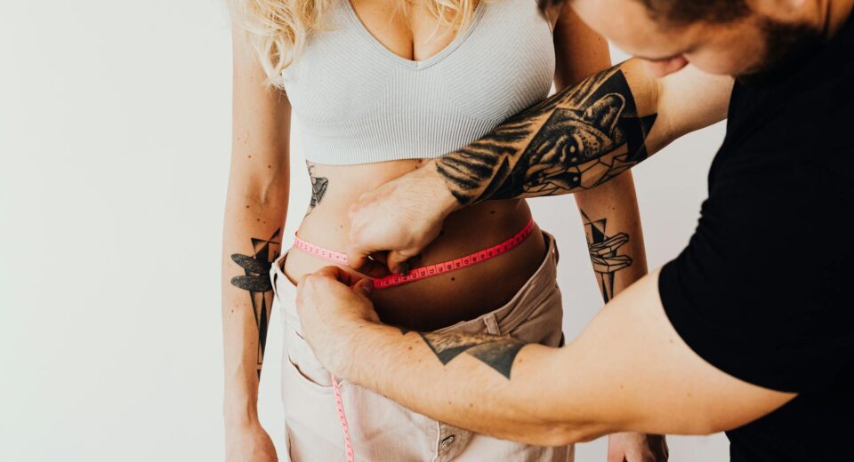 A man measures a woman's waist with a tape measure, focusing on fitness and health goals.