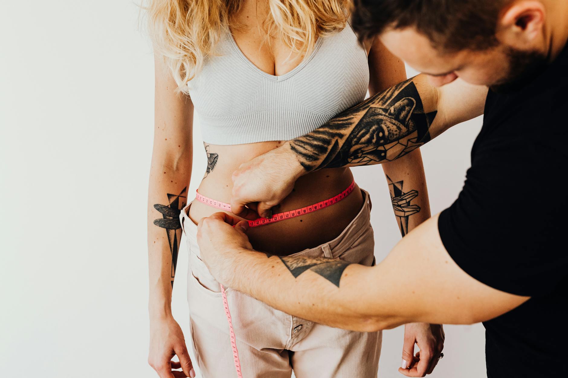 A man measures a woman's waist with a tape measure, focusing on fitness and health goals.