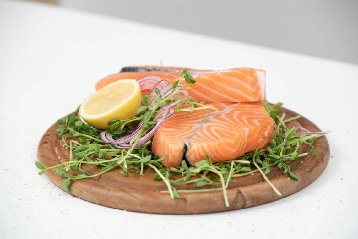 Close-up of fresh salmon slices with lemon and microgreens on a wooden platter. Ideal for food-related themes.