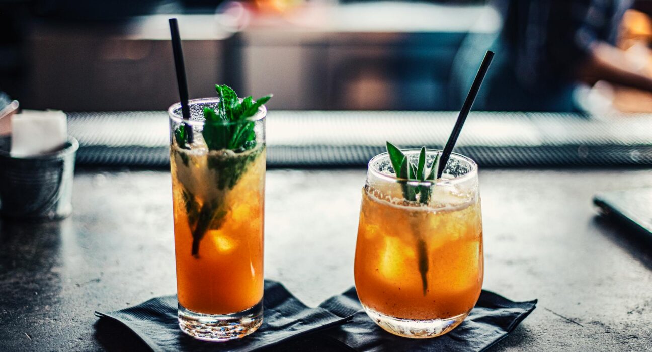 Two chilled cocktails with mint and ice on a bar counter, garnished with fresh mint leaves.