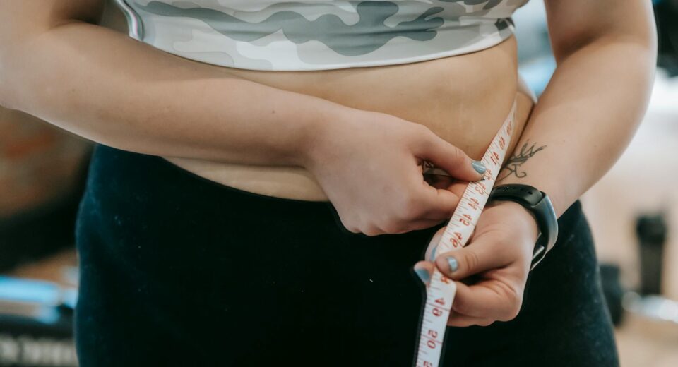 Crop anonymous plus size female with measuring tape measuring waist on blurred background