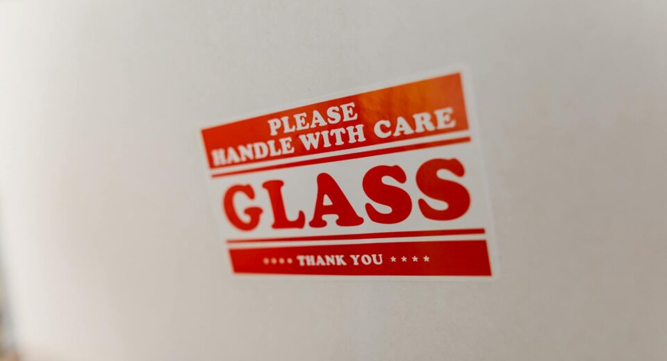 Close-up of a glass packaging label with 'Handle with Care' warning text on a white box.