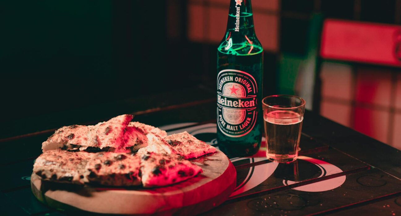 Cozy indoor setting with Heineken beer and pizza on a wooden table, perfect for casual dining.