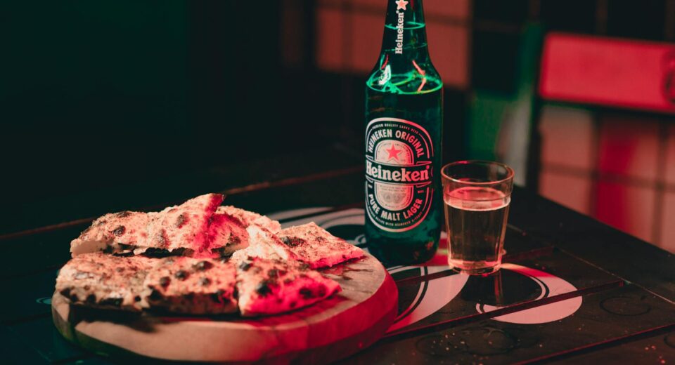 Cozy indoor setting with Heineken beer and pizza on a wooden table, perfect for casual dining.