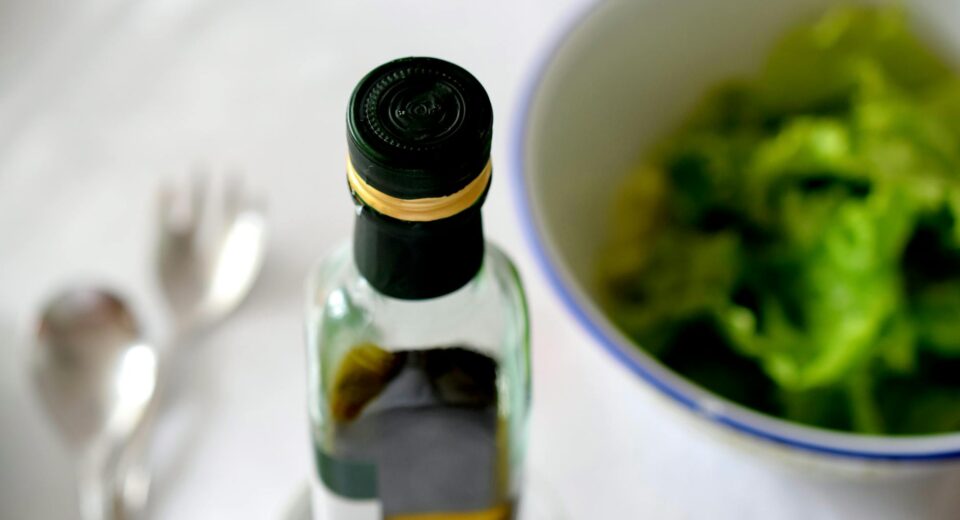 A high-angle view of an olive oil bottle alongside a fresh green salad and cutlery.