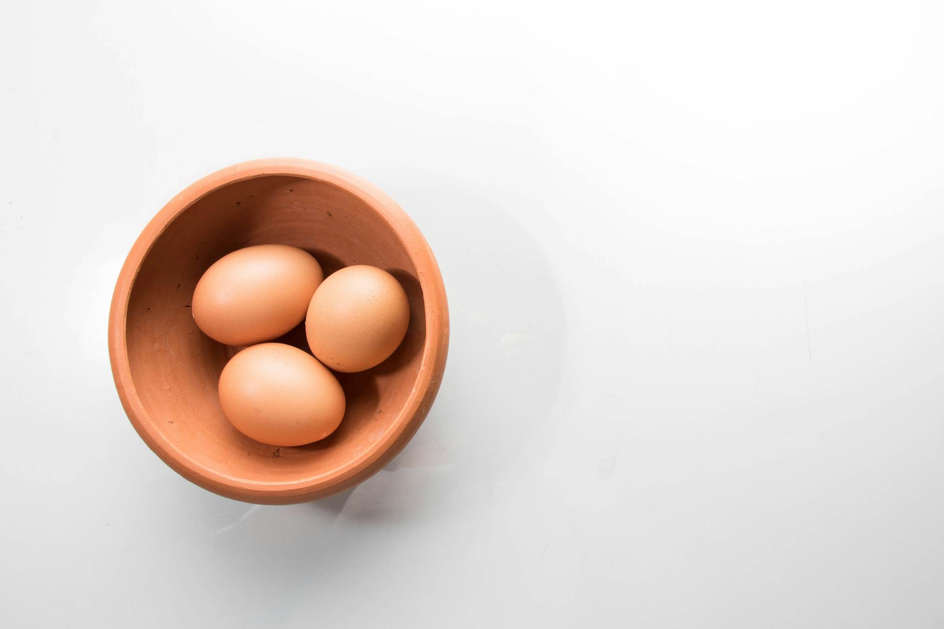 A top-down view of three brown eggs in a brown ceramic bowl on a white background.