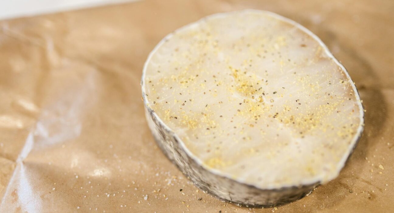 High-quality image of a raw fish fillet with seasoning placed on paper, ready for cooking.