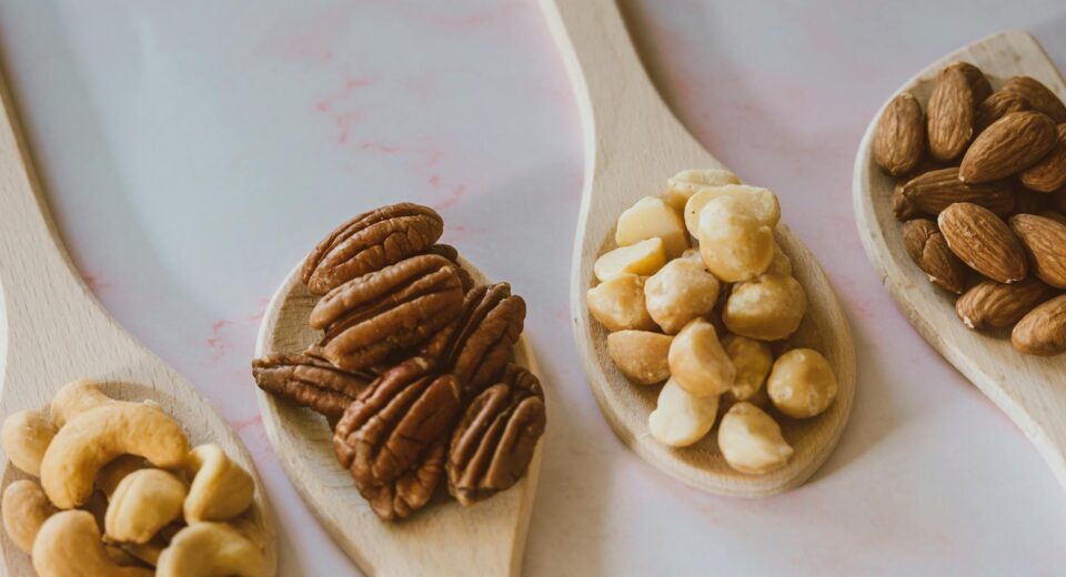 Close-up of assorted nuts like almonds, pecans, cashews, and macadamia on wooden spoons.