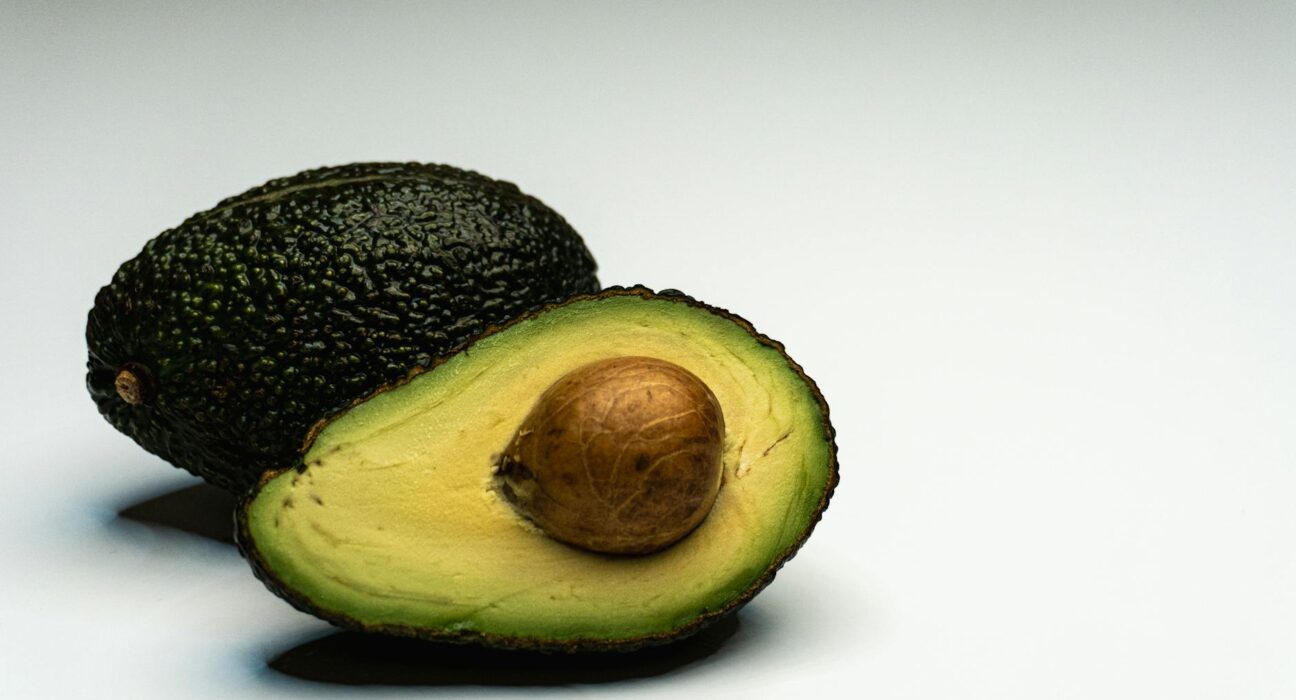 Close-up of a sliced avocado displaying its vibrant green flesh and seed on a white background.