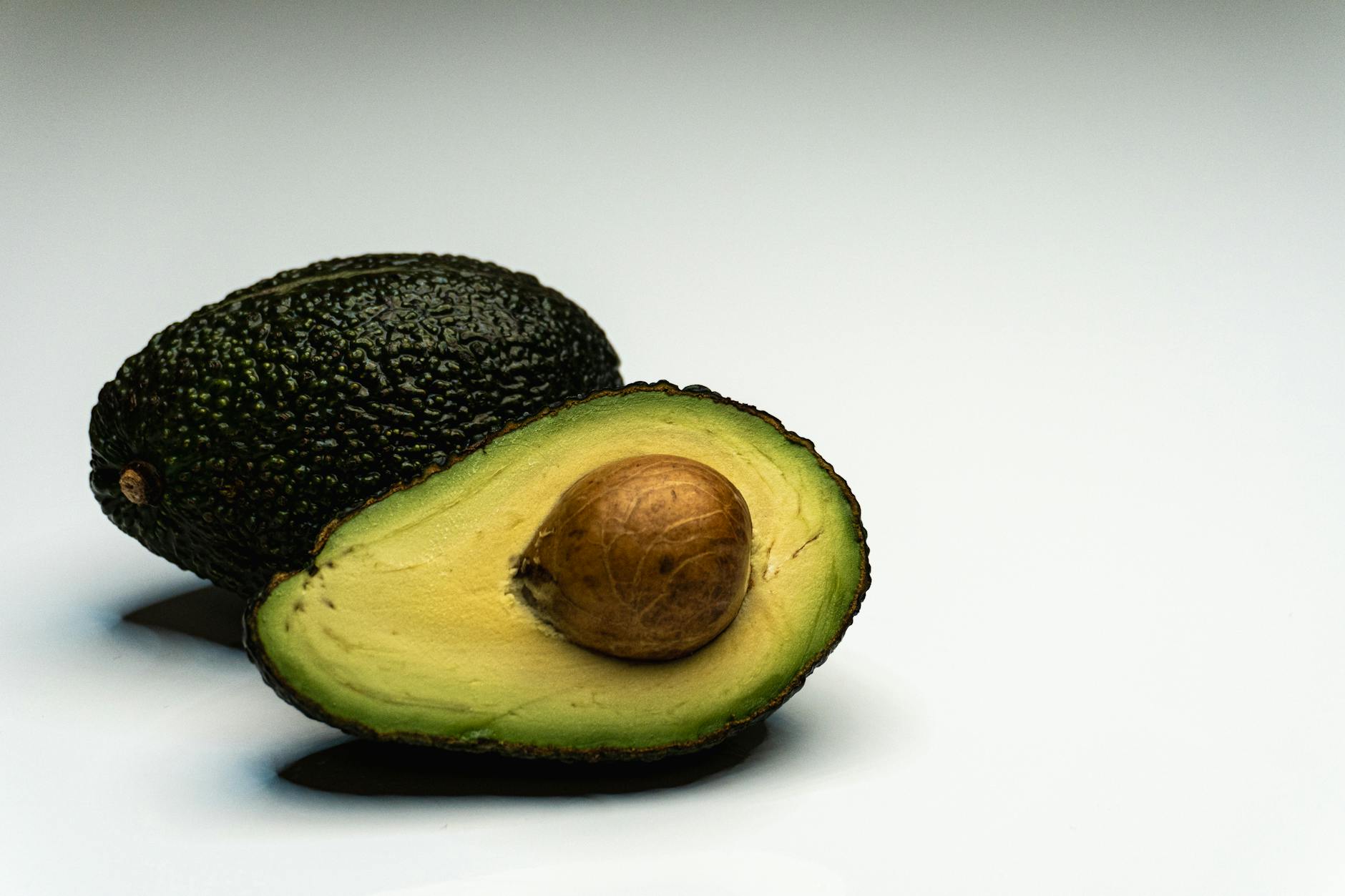 Close-up of a sliced avocado displaying its vibrant green flesh and seed on a white background.