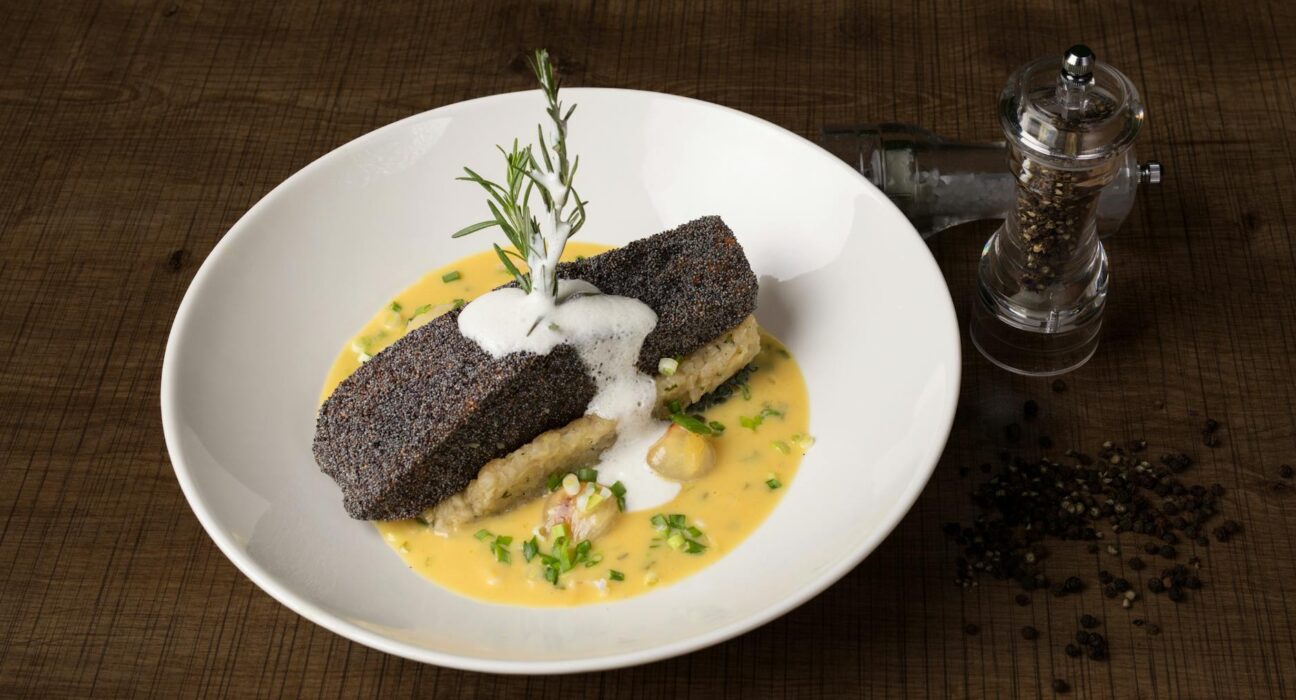 A high-angle shot of popcorn crusted fish with creamy sauce, presented on a wooden table.