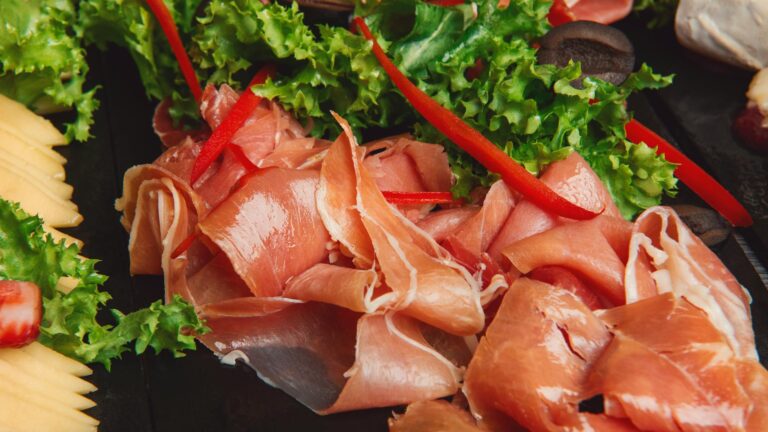 Close-up of prosciutto with fresh lettuce and red bell peppers, perfect for gourmet food lovers.