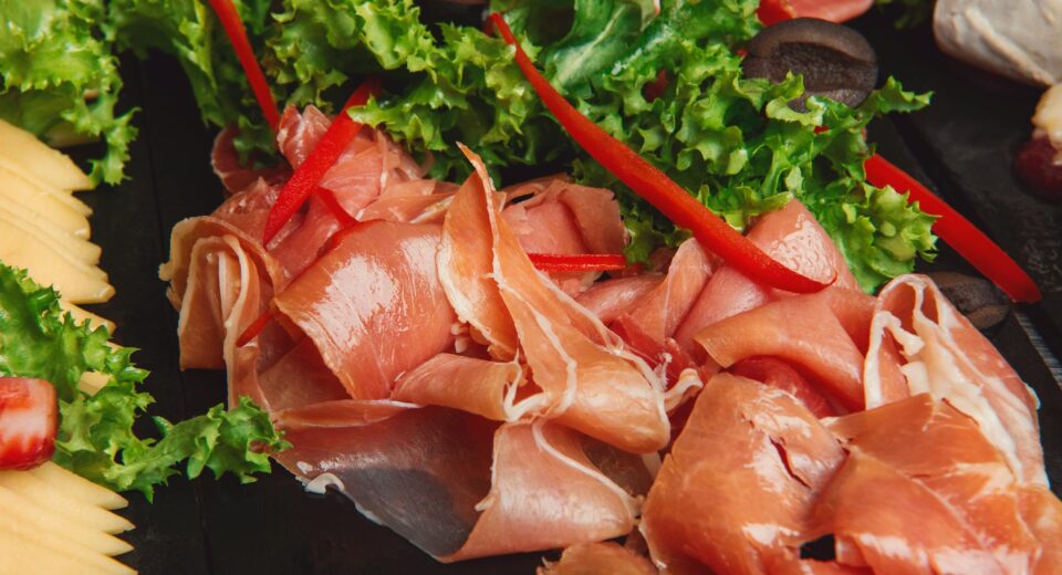 Close-up of prosciutto with fresh lettuce and red bell peppers, perfect for gourmet food lovers.