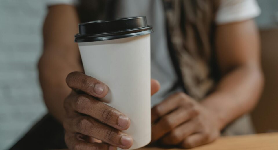 Hand holding a white disposable takeaway coffee cup with black lid, close-up view.