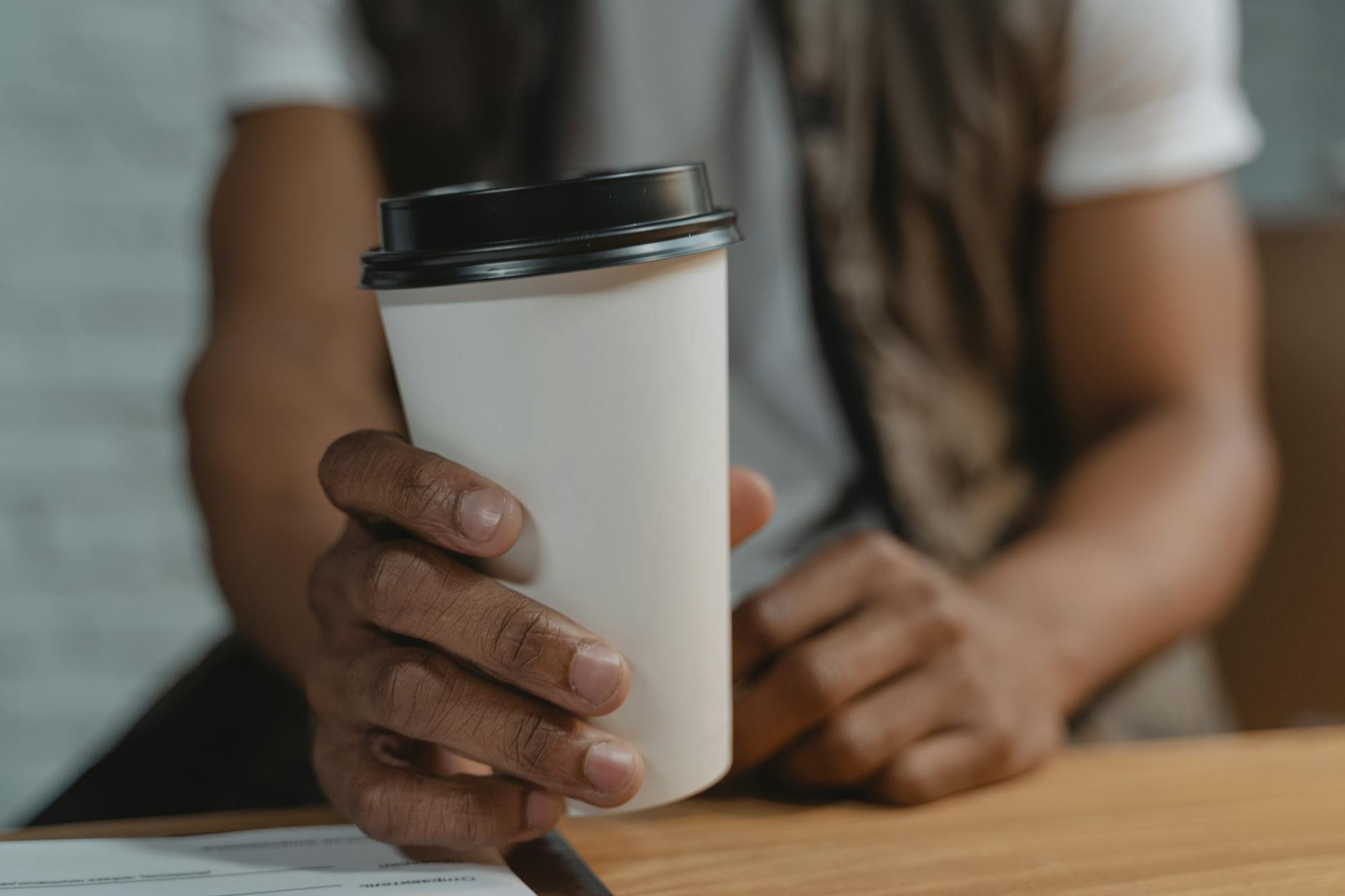 Hand holding a white disposable takeaway coffee cup with black lid, close-up view.