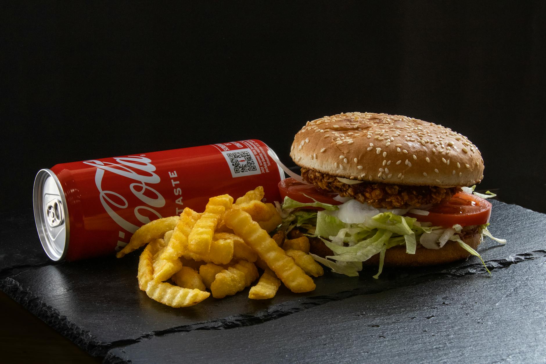 Tasty crispy chicken burger with fresh fries and a soda, perfect for a fast-food craving.