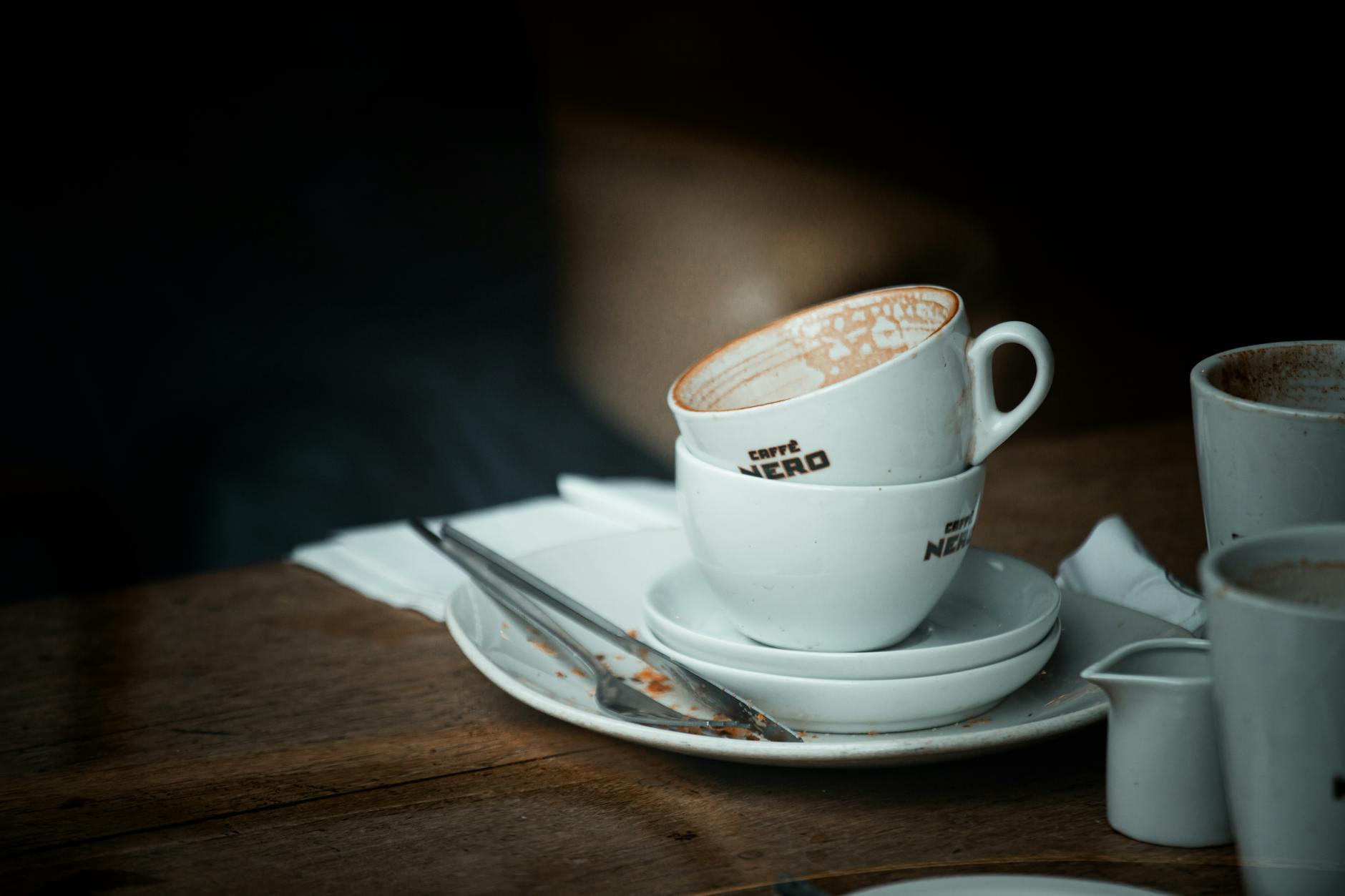 Stacked ceramic coffee cups on a wooden table in a cozy café setting, highlighting vintage café culture.