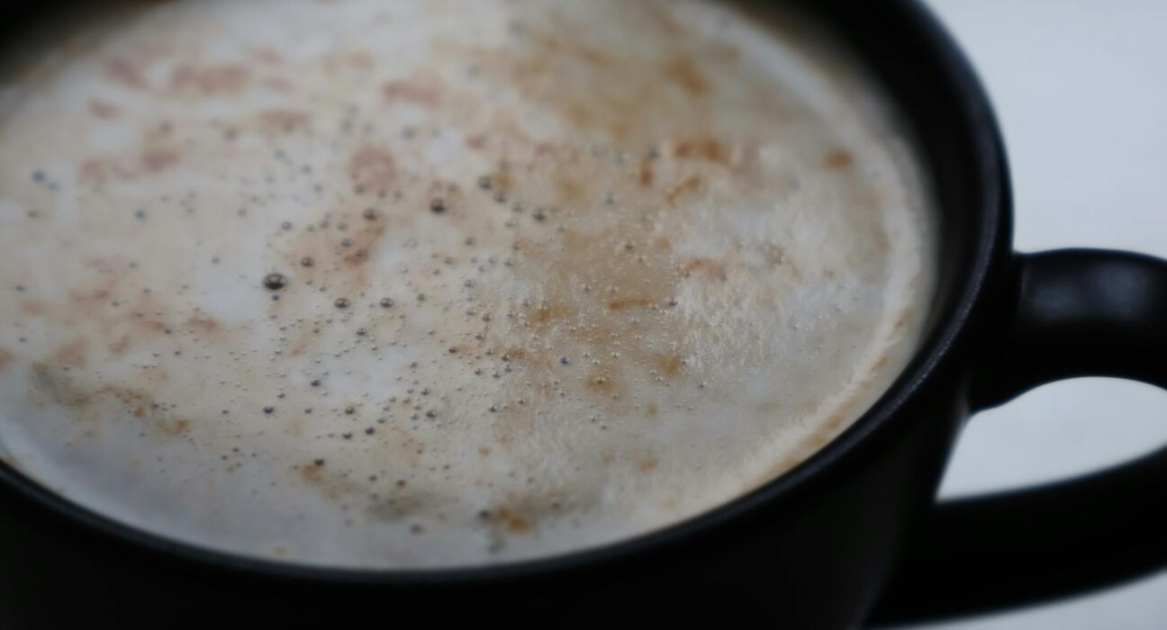 A detailed close-up of a frothy cappuccino in a matte black mug, showcasing coffee textures.