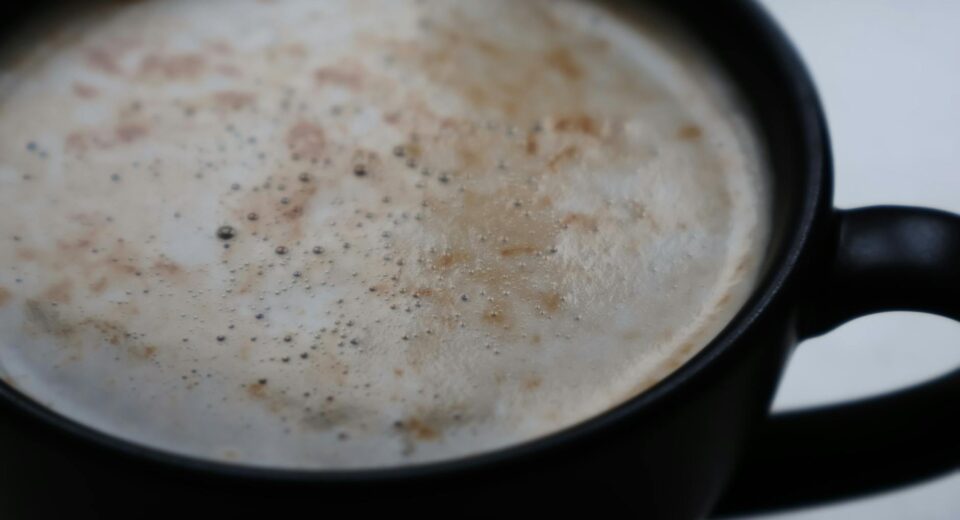 A detailed close-up of a frothy cappuccino in a matte black mug, showcasing coffee textures.