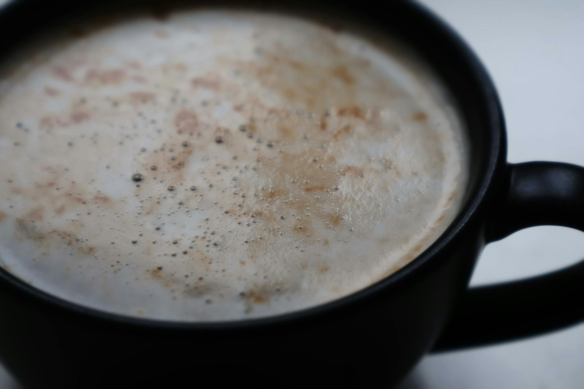 A detailed close-up of a frothy cappuccino in a matte black mug, showcasing coffee textures.
