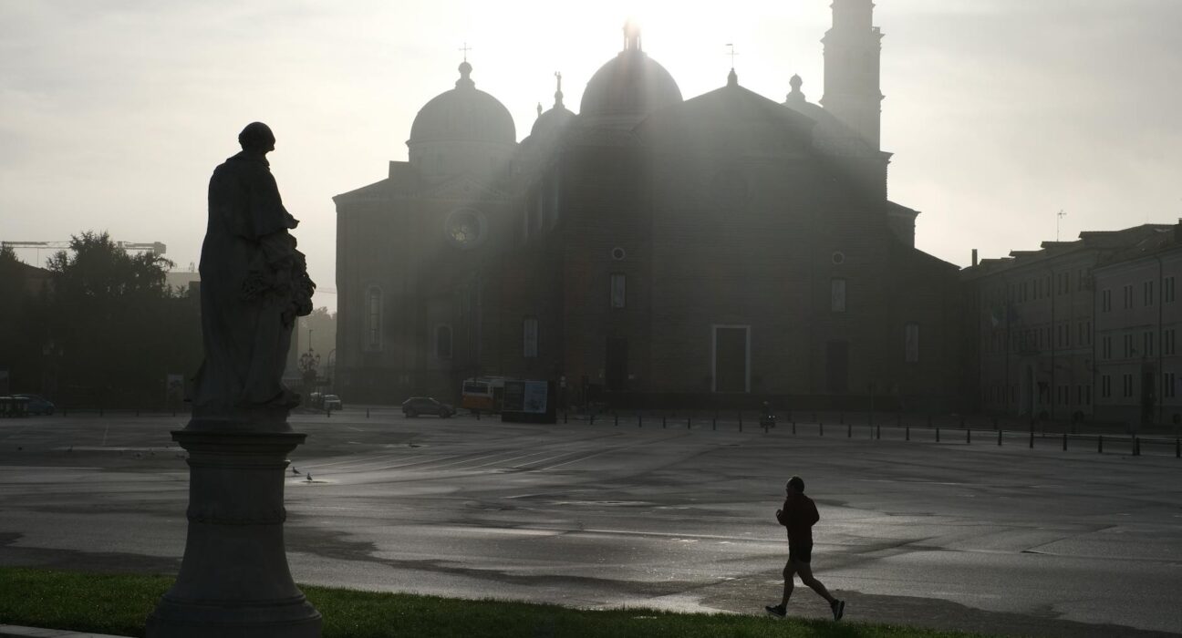 A jogger silhouettes against a misty European piazza with a historic church at sunrise.
