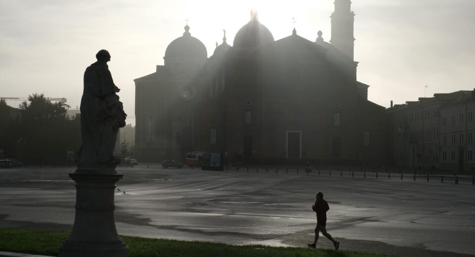 A jogger silhouettes against a misty European piazza with a historic church at sunrise.