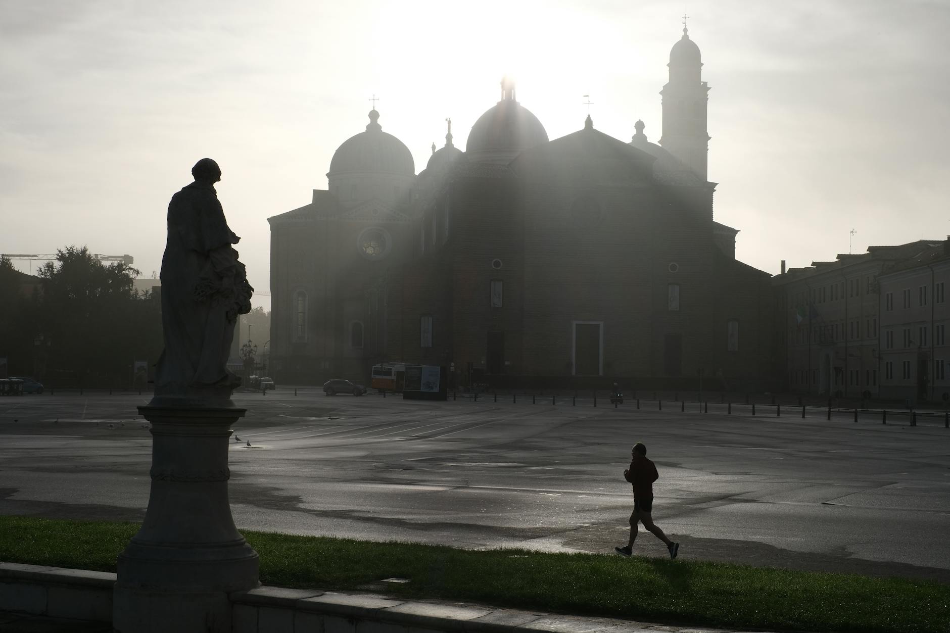 A jogger silhouettes against a misty European piazza with a historic church at sunrise.