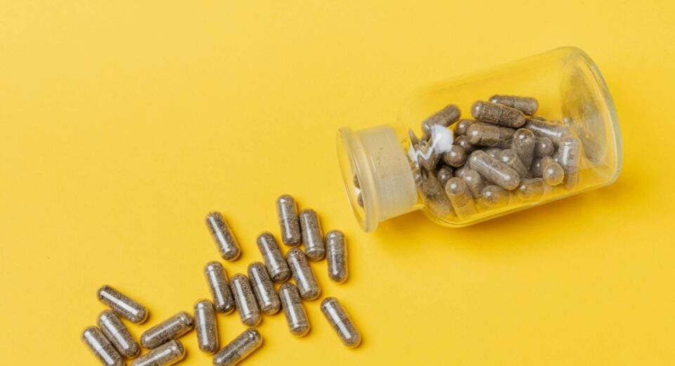 A glass bottle spilling capsules on a vivid yellow background. Perfect for healthcare and medicine themes.