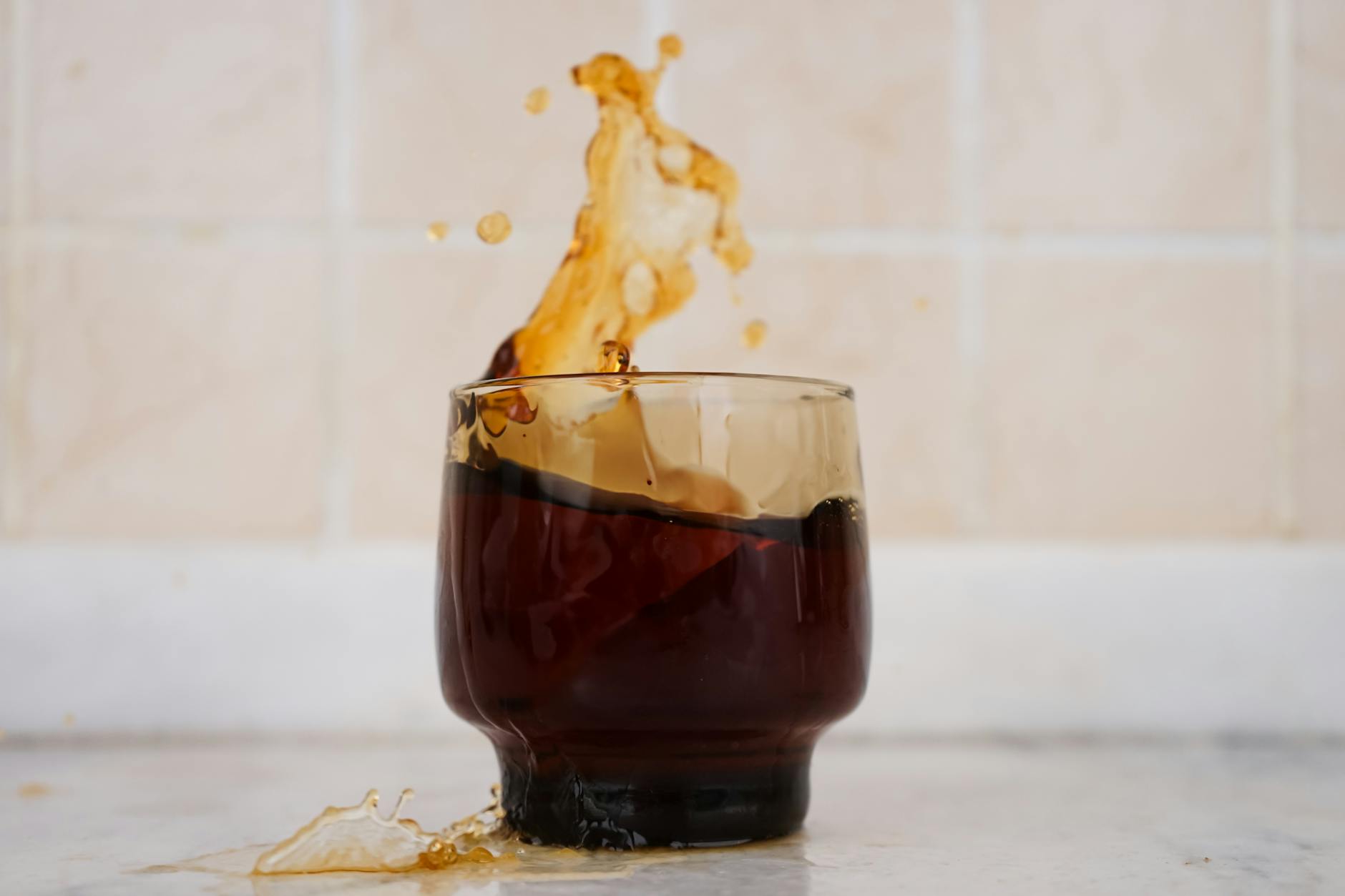 Energetic splash of coffee in a clear glass against a tiled background, capturing motion and excitement.