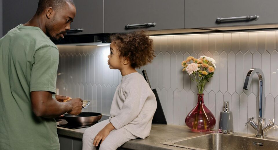 A father and daughter bonding while cooking together in a modern kitchen.