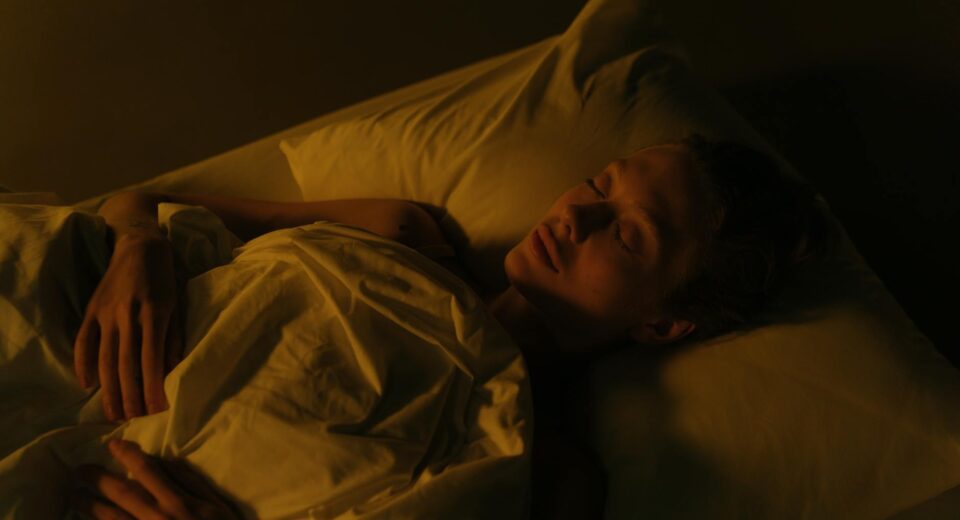 A woman peacefully sleeping in a dimly lit bedroom, wrapped in a white blanket.