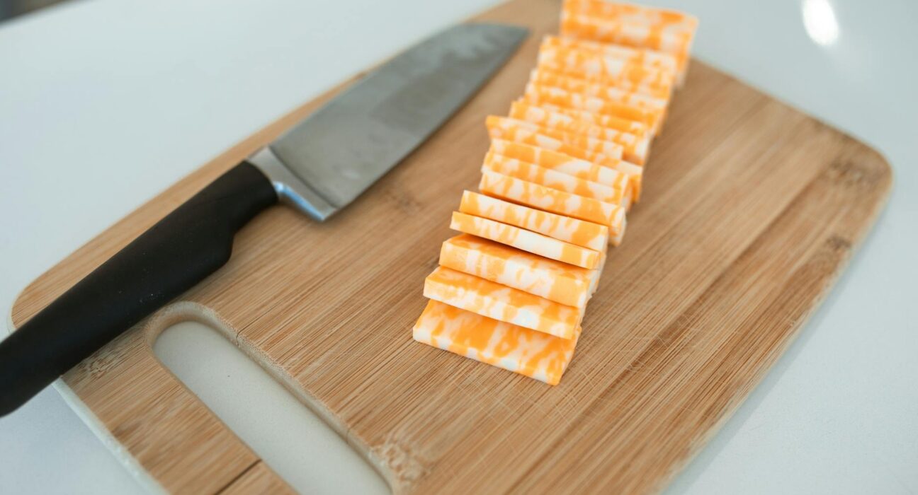 Sliced colby-jack cheese neatly arranged on a bamboo cutting board with a kitchen knife.