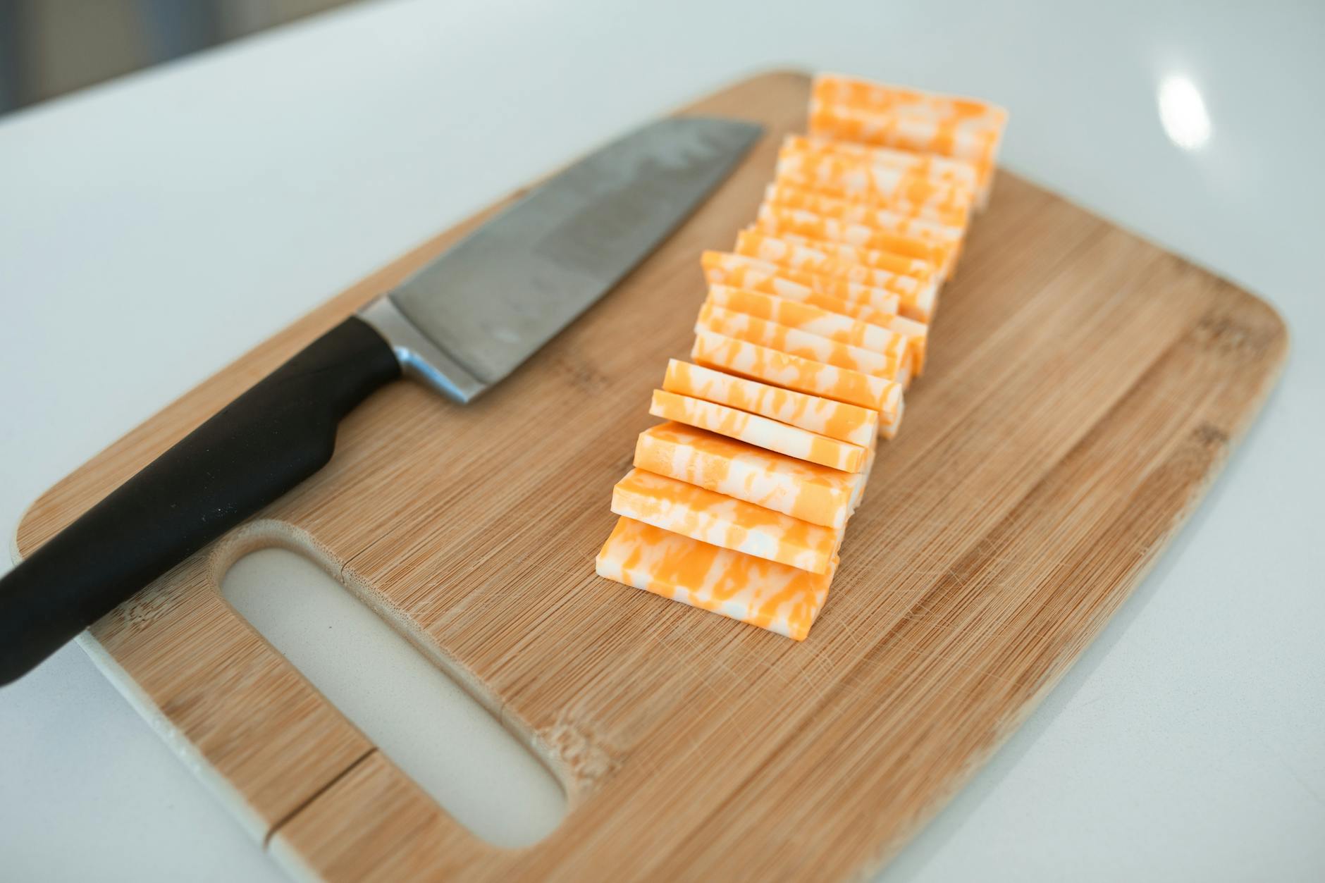 Sliced colby-jack cheese neatly arranged on a bamboo cutting board with a kitchen knife.
