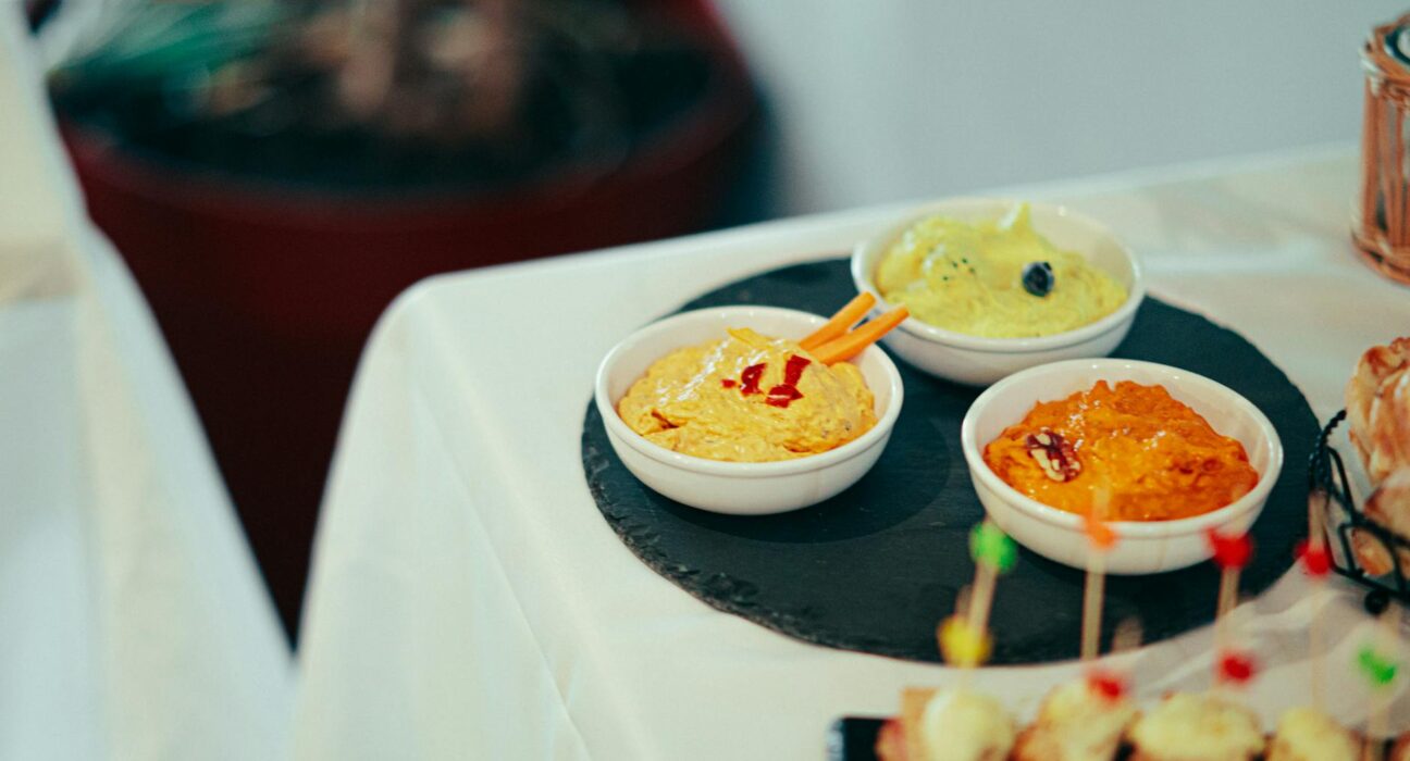 A variety of colorful dips served in bowls on a slate platter at a buffet table.