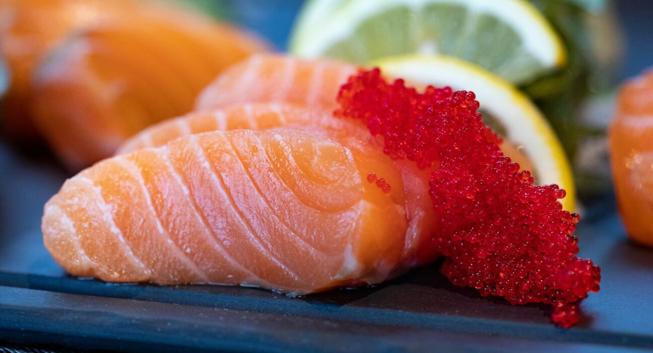 Close-up of fresh salmon sashimi topped with bright red caviar and garnished with lemon slices.