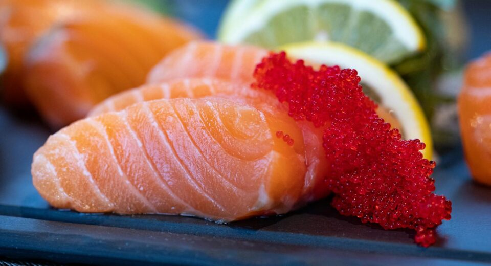Close-up of fresh salmon sashimi topped with bright red caviar and garnished with lemon slices.