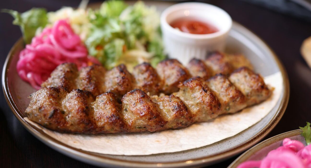 A plate of succulent grilled kebab served with fresh salad and sauce, perfect for food lovers.