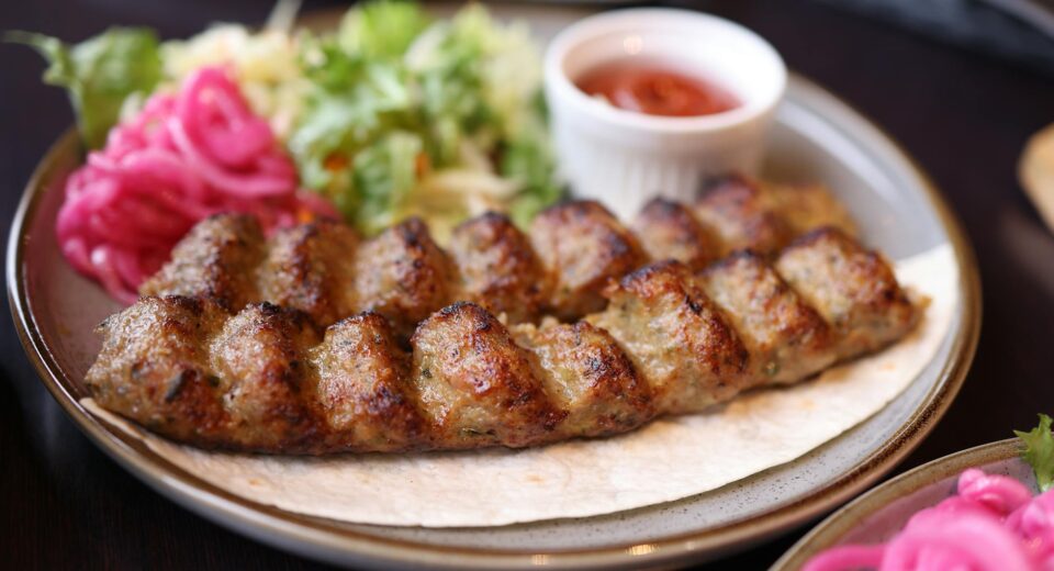 A plate of succulent grilled kebab served with fresh salad and sauce, perfect for food lovers.