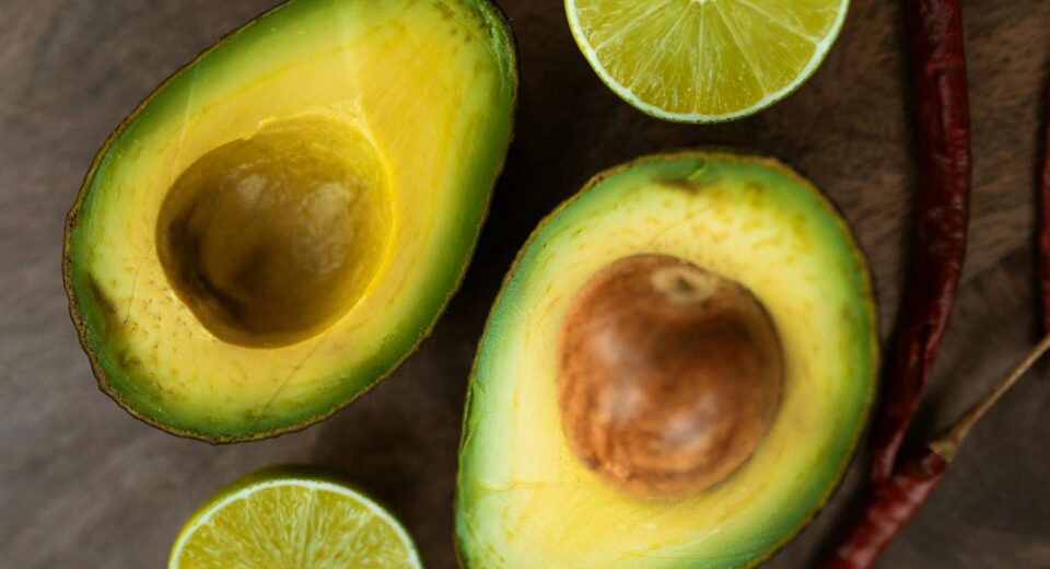 Sliced avocado and lime with chili peppers on a wooden background, perfect for culinary themes.