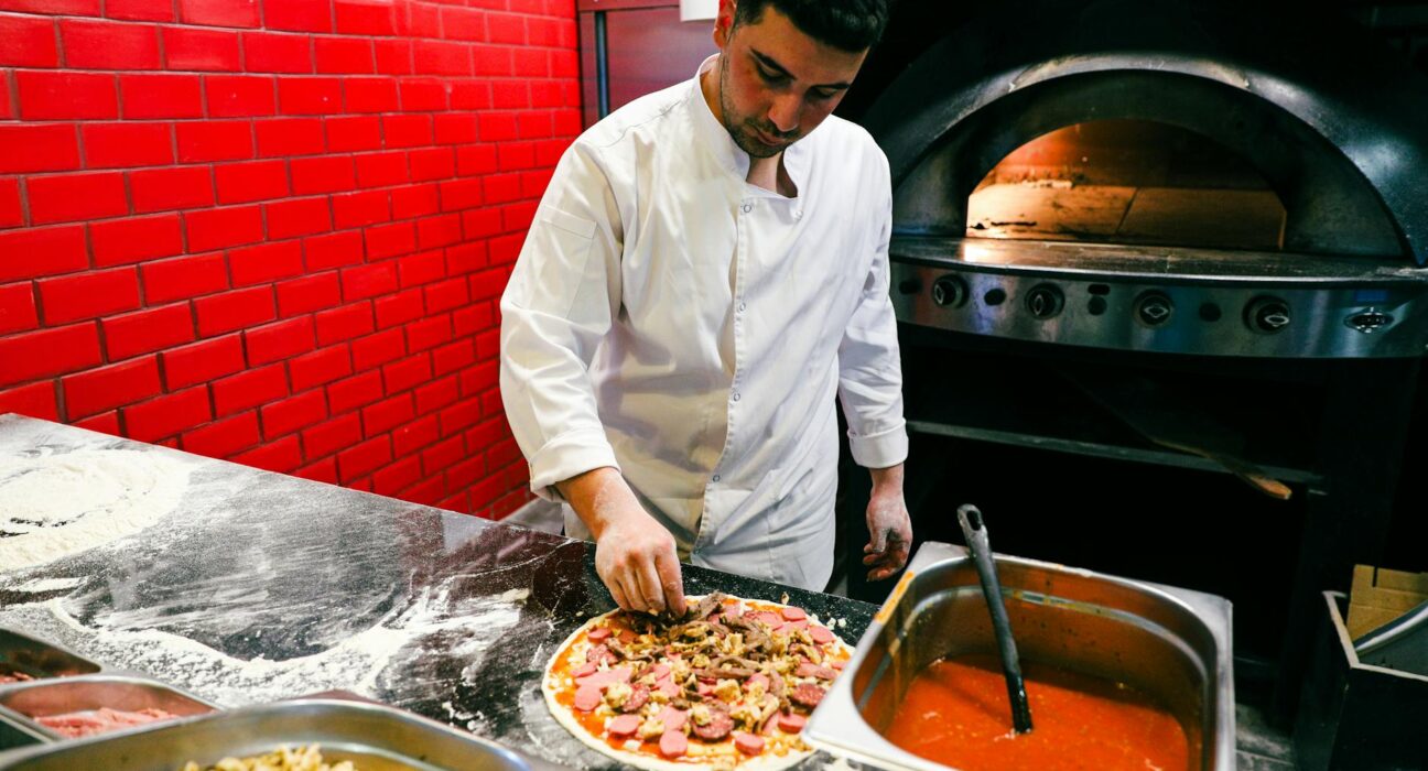 Chef in white uniform preparing pizza in a brick oven kitchen. Italian cuisine and culinary art.