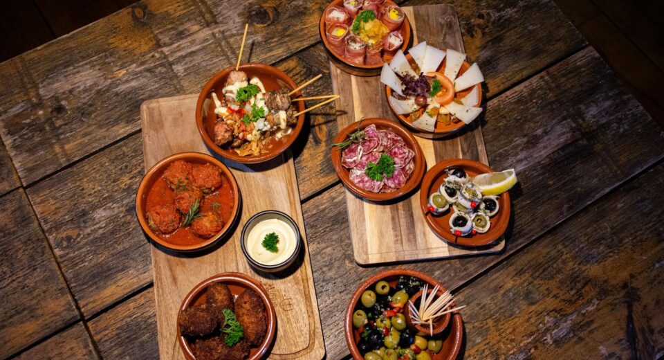 An inviting flat lay of diverse gourmet tapas on a wooden table, perfect for a rustic dining experience.