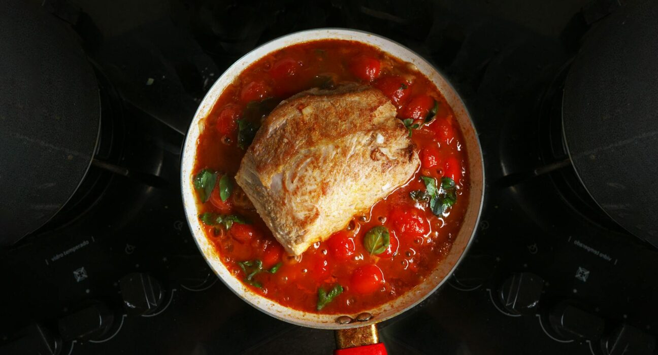 A savory roast beef cooked in rich tomato sauce with herbs, atop a stovetop.