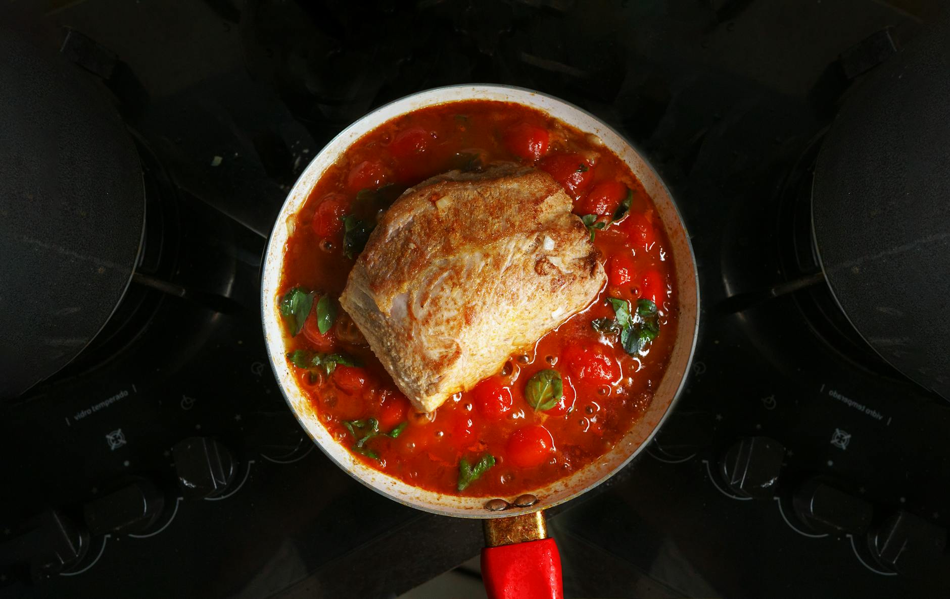 A savory roast beef cooked in rich tomato sauce with herbs, atop a stovetop.