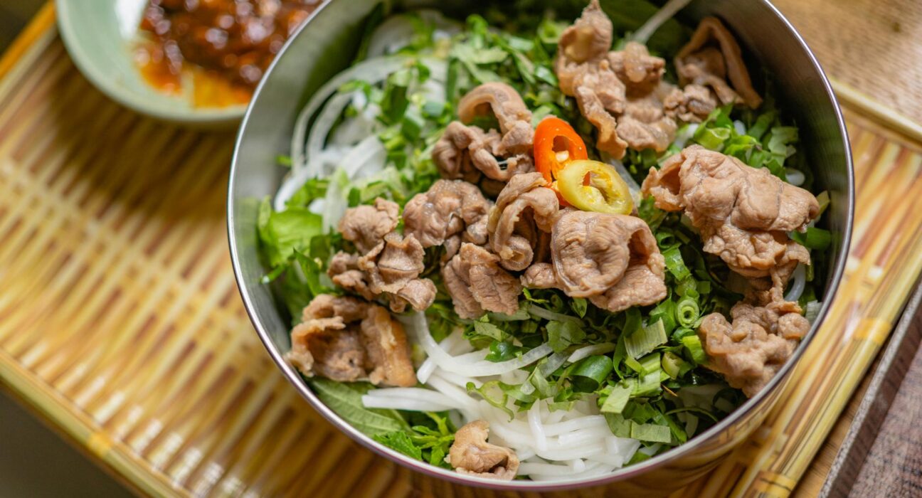 Tantalizing pho bowl filled with fresh herbs, tender beef slices, and vibrant chilies on a bamboo mat.
