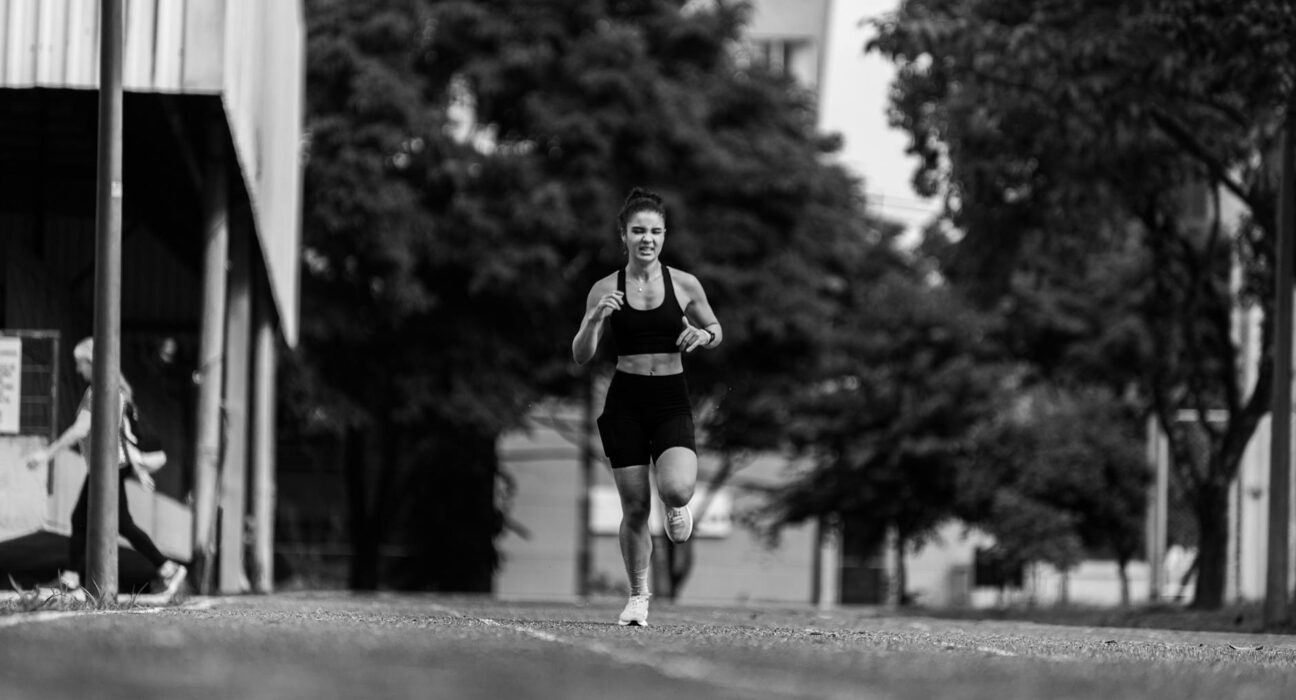 A young woman runs energetically outdoors, captured in a dynamic black and white photo.