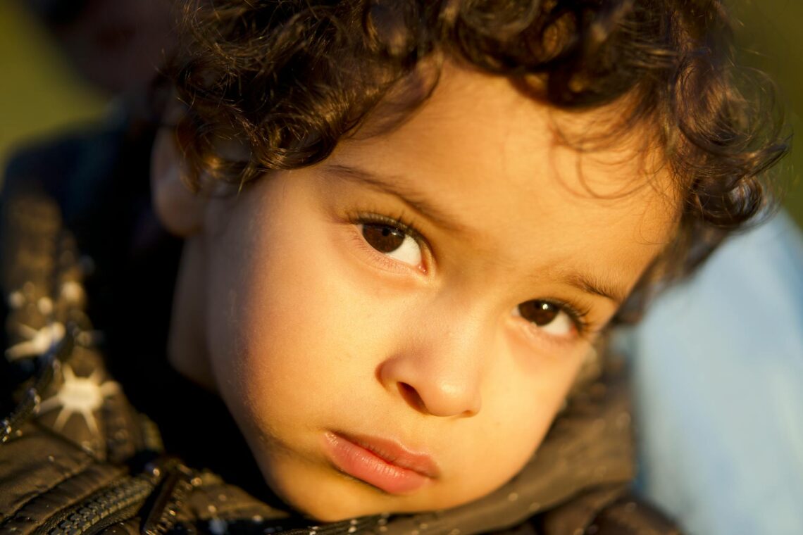 Captivating portrait of a young child with curly hair looking thoughtful in golden lighting.