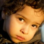 Captivating portrait of a young child with curly hair looking thoughtful in golden lighting.
