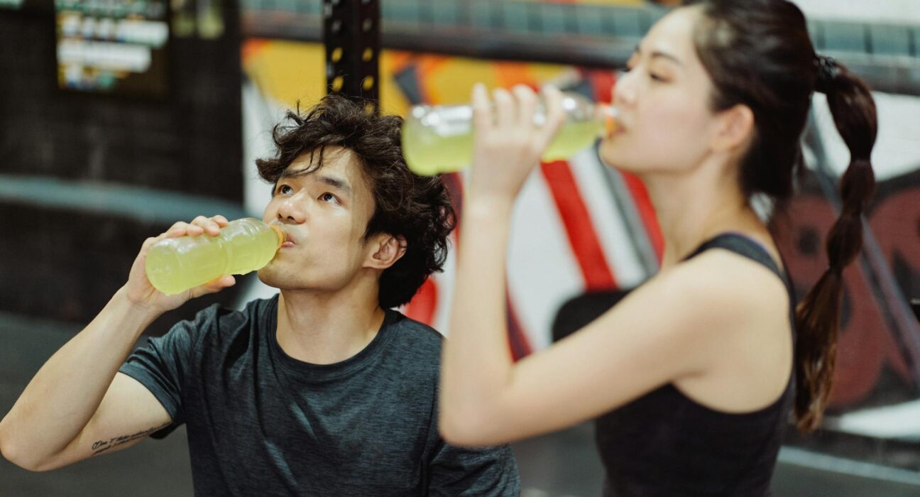 Fit Asian couple hydrating at the gym after an intense workout. Refreshing drink break.