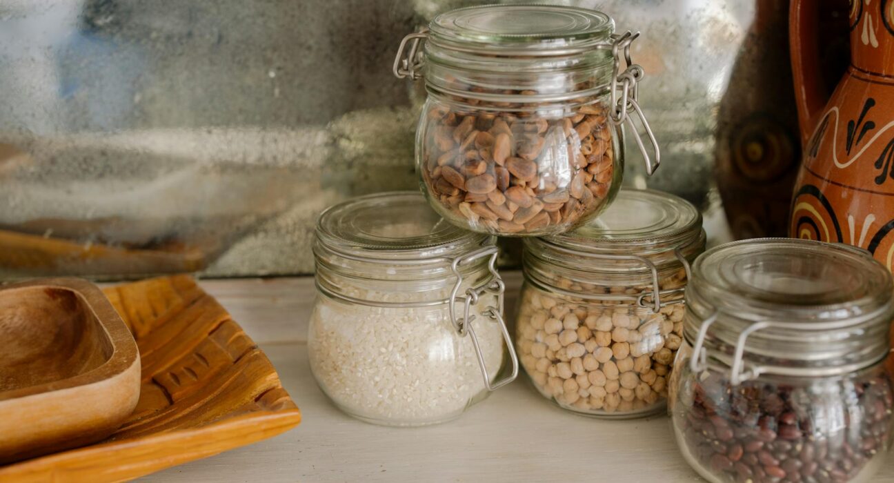 Elegant kitchen scene with glass jars of chickpeas, rice, and beans on a wooden counter.