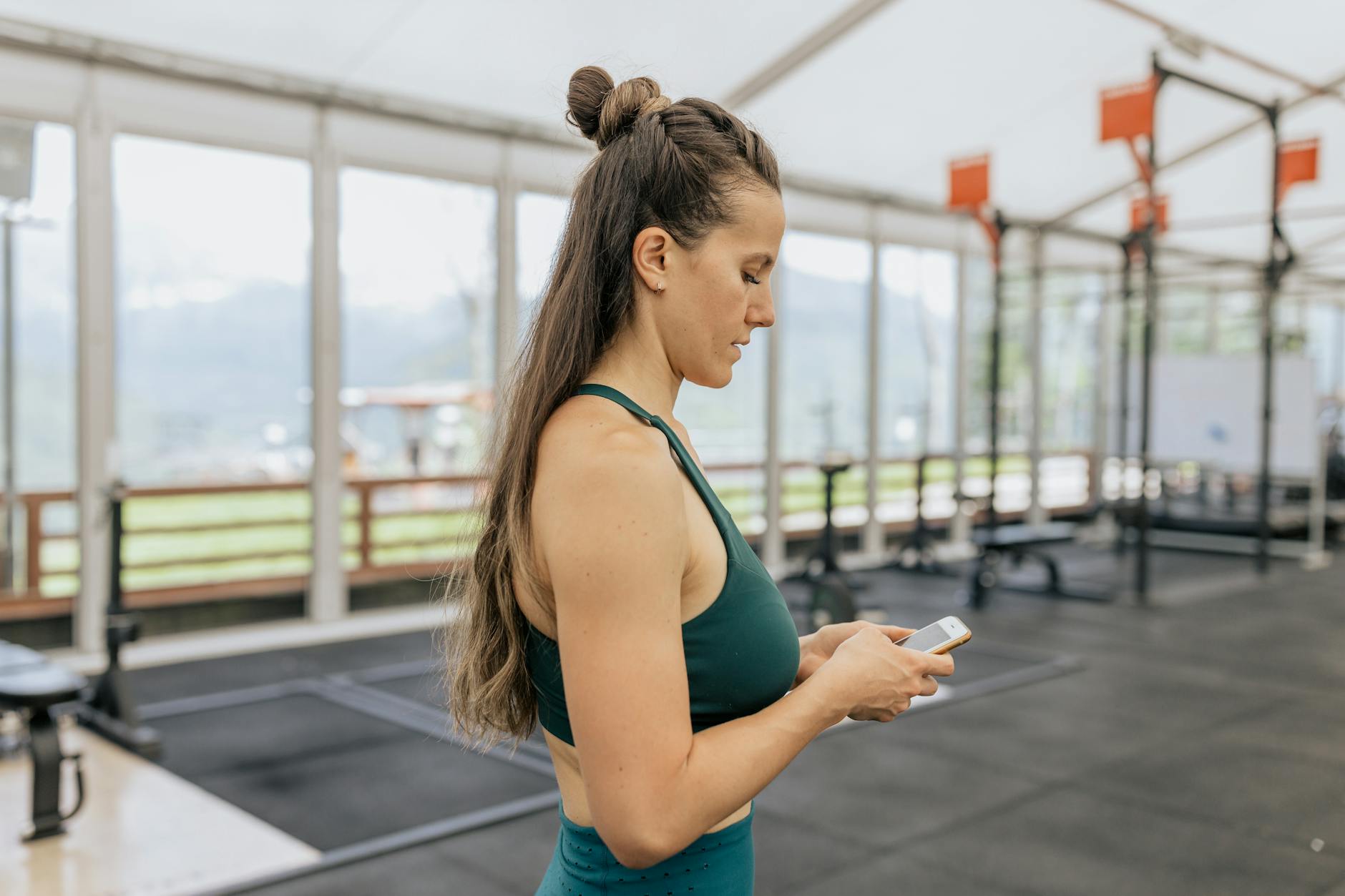 Female athlete in gym looking at phone, dressed in activewear for training.